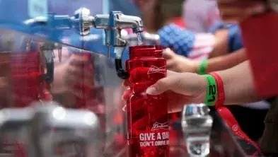 Hand at a water filling station filling up a red reusable waterbottle