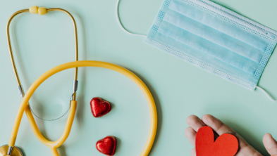 stethoscope and mask and a hand holding a red felt heart