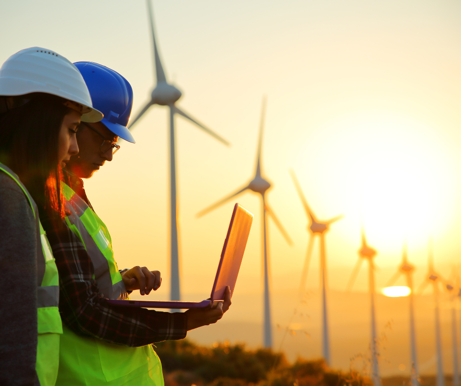 A student and professor stand under a line of windmills with a laptop at dawn